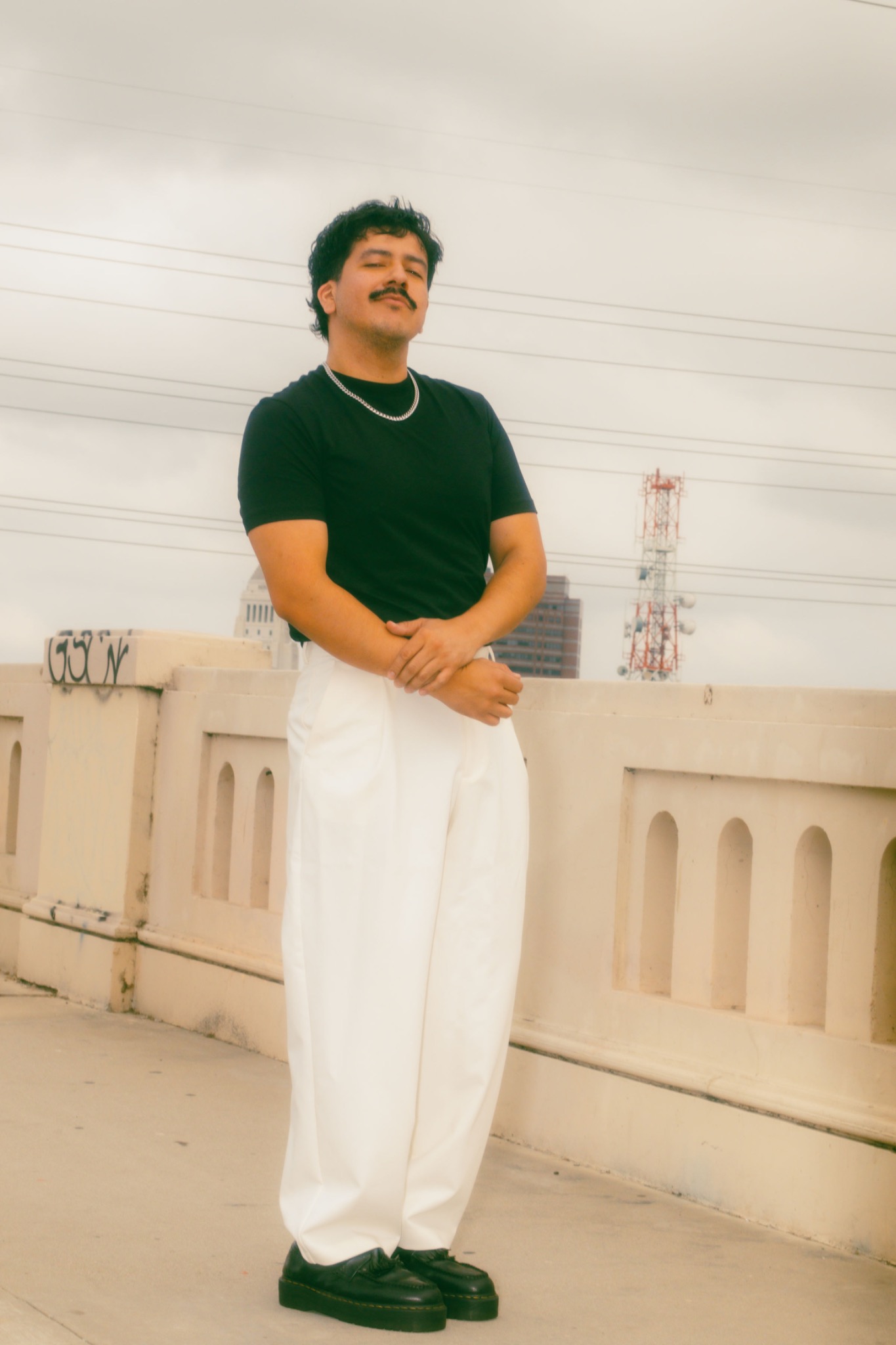 Saul Aroche standing on a rooftop in a black shirt and cream trousers